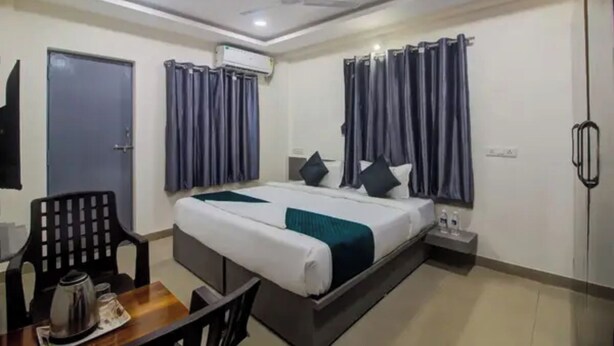 Habitación de hotel con cama, escritorio, silla, cafetera y mesita de noche con lámpara.