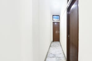 A narrow hallway with a wooden door at the end, a tiled floor, and a small window with a view of the sea.