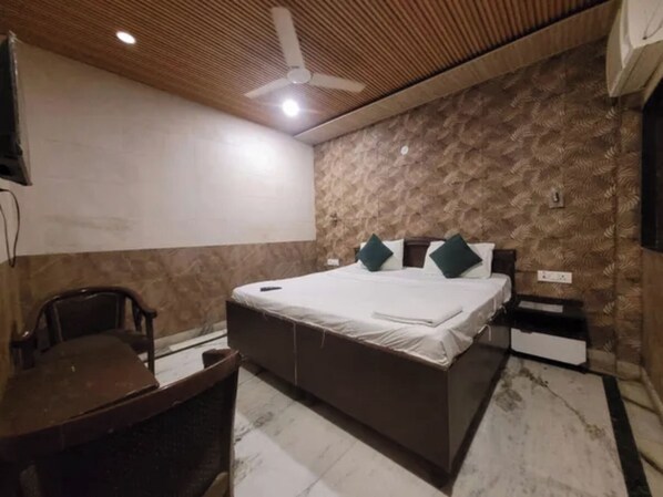 A bedroom with a bed, a desk, a chair, a ceiling fan, and a patterned wall.