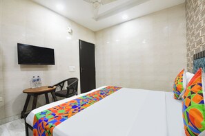 A hotel room with a bed, a television mounted on the wall, a small table with a chair, and a door. - FabHotel Metro Inn Kalkaji (New Delhi)