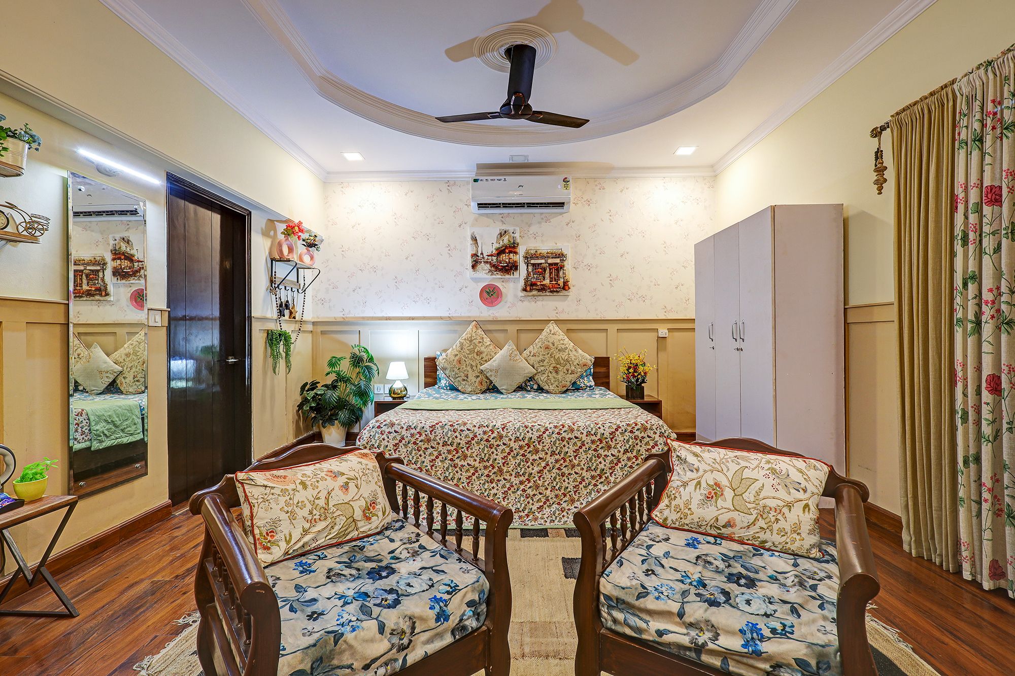 A bedroom with a bed, two chairs, a wardrobe, a ceiling fan, and wall-mounted air conditioning.