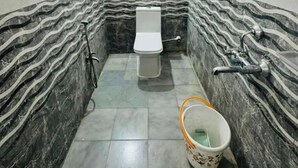 A bathroom with a toilet, a shower area, and a bucket on the floor. - Fabhotel Svr Inn (Hyderabad)