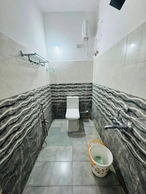 Un baño con inodoro, zona de ducha y un cubo en el suelo.