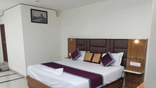 A neatly made bed with a headboard, a bedside table, and a wall-mounted shelf. - Fabhotel Svr Inn (Hyderabad)