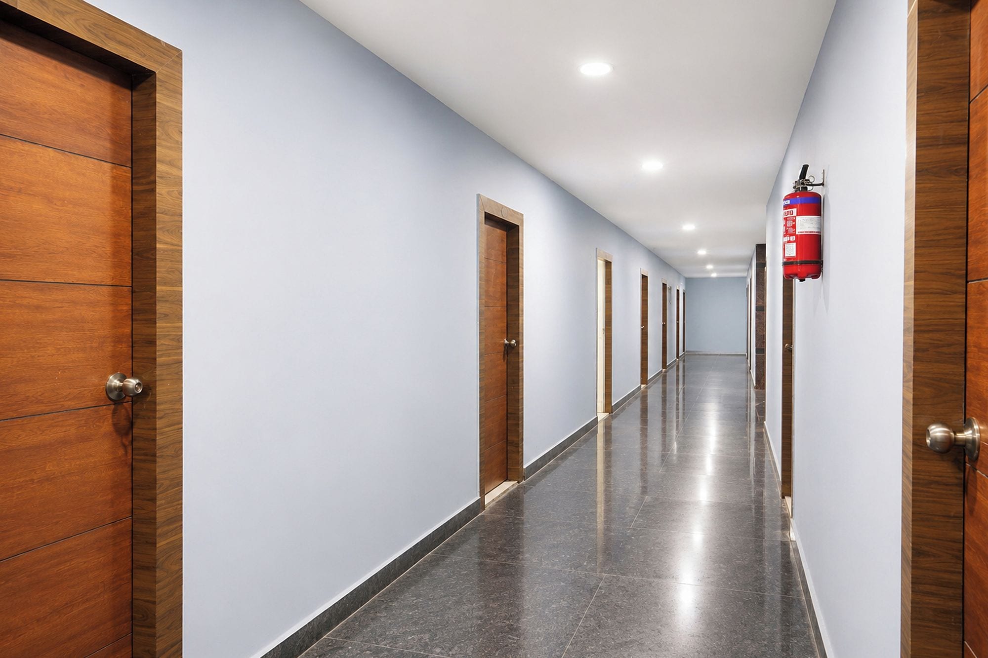 Un couloir avec des portes en bois d’un côté et un extincteur fixé au mur.