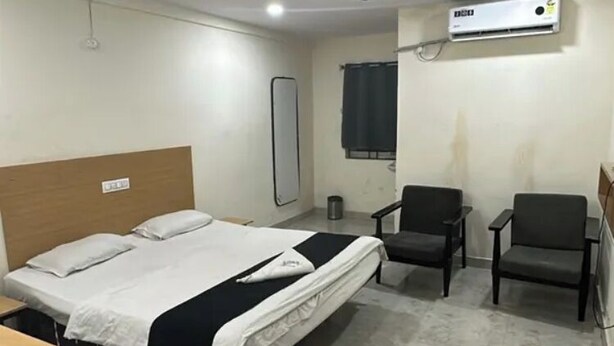 A hotel room with a bed, two chairs, a ceiling fan, and an air conditioning unit.