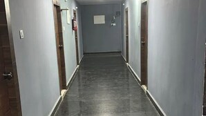 A long, narrow hallway with doors on both sides, leading to individual rooms. The floor is dark, and the walls are painted a light color.