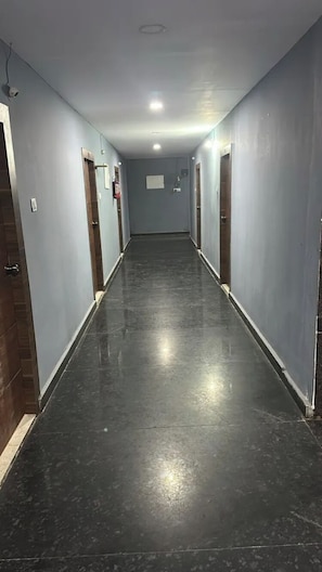 A long, narrow hallway with doors on both sides, leading to individual rooms. The floor is dark, and the walls are painted a light color.