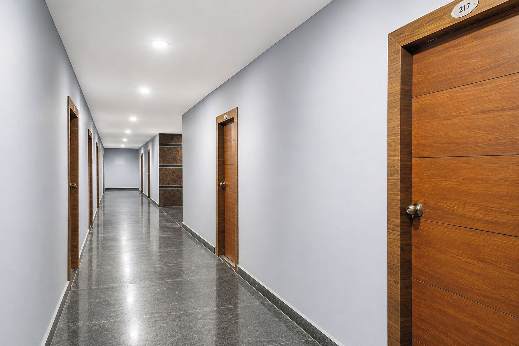 Un long couloir étroit, doté d’un plancher poli, de portes en bois et du numéro « 217 » sur la porte de droite.