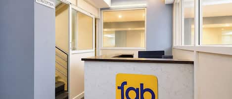 A reception desk with a sign for 'fab hotels', a ceiling fan, and a staircase leading to another area.