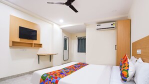 Una habitación de hotel con cama, televisor montado en la pared, equipo de aire acondicionado y ventilador de techo.