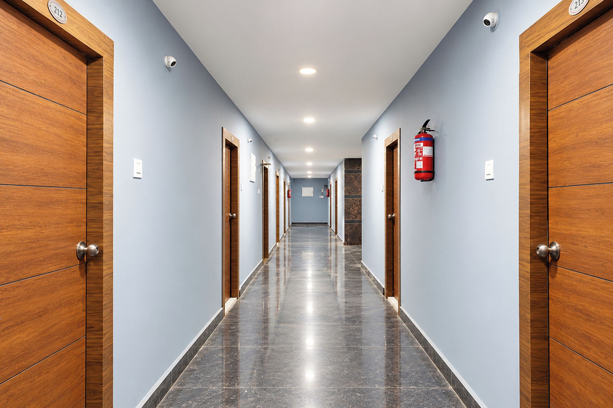 A hotel hallway with wooden doors, a fire extinguisher, and a fire alarm on the wall.