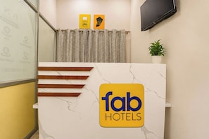 Una recepción con encimera de mármol, el logotipo de 'fab hotels' y una planta en maceta en la pared.