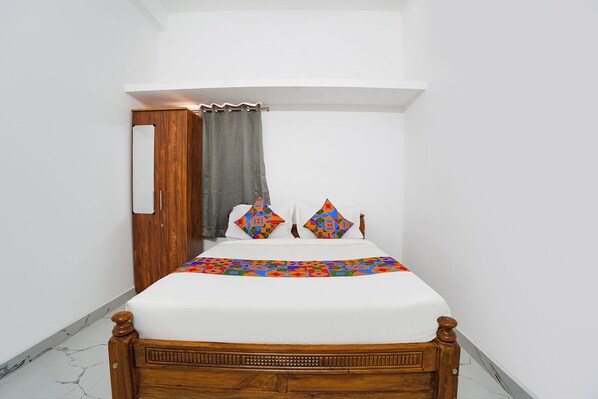 A bedroom with a wooden bed, white bedding, and colorful geometric pillows.