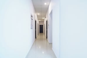 En lång, smal hall med vita väggar och ett kaklat golv, som leder fram till en mörk dörr längst ner.