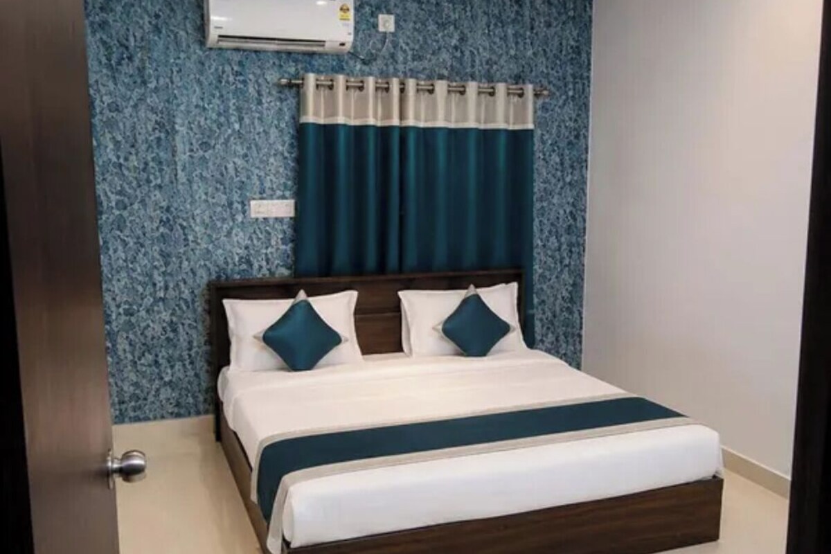 A hotel room with a bed, a ceiling fan, an air conditioning unit, and a window with curtains.