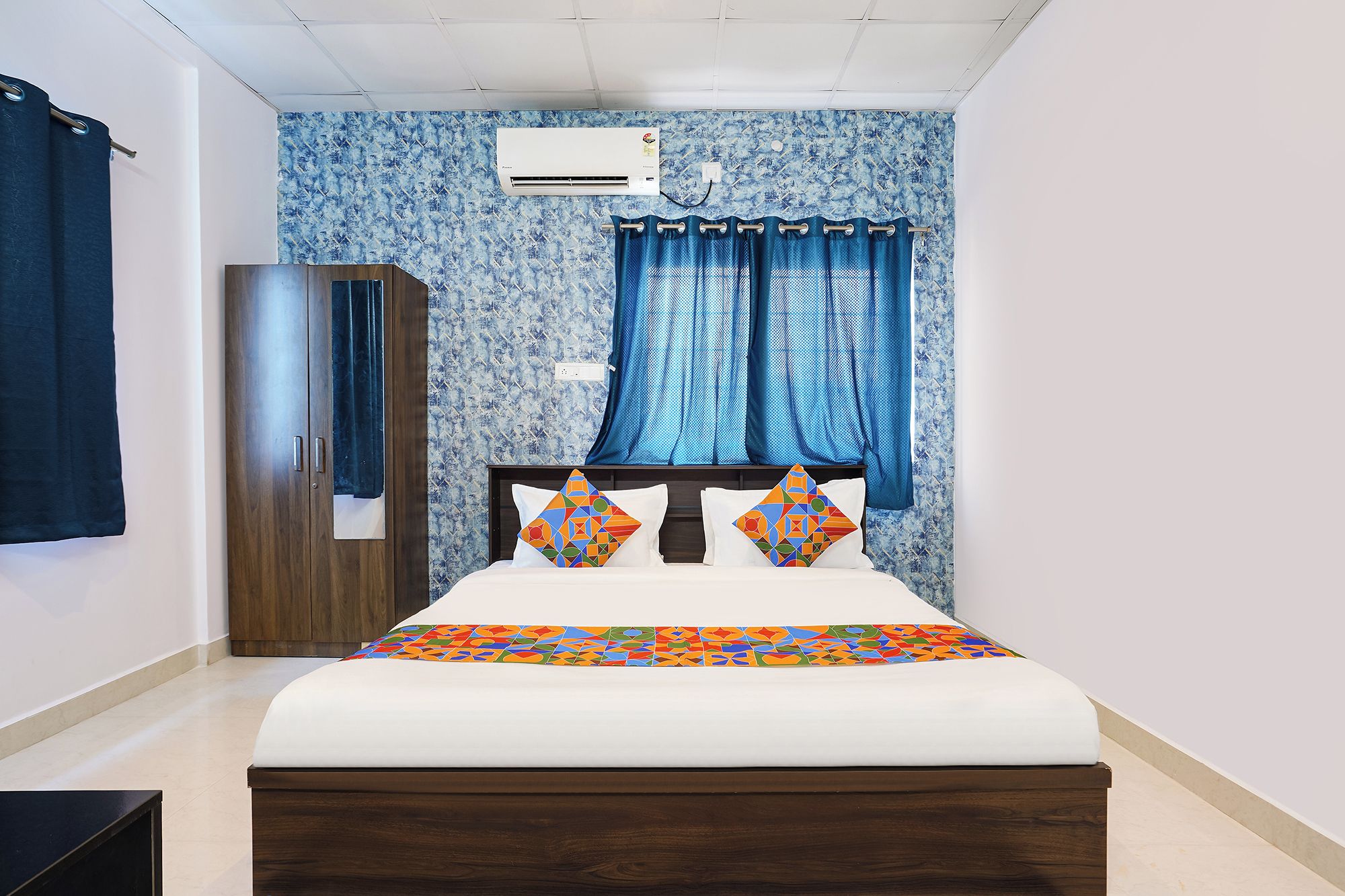 Een slaapkamer met een bed, een kledingkast, een raam met gordijnen en een airconditioning.