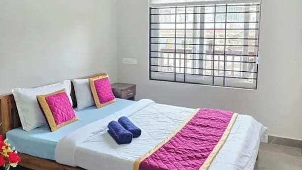 A single bed with a headboard, a window with metal bars, and a ceiling fan.