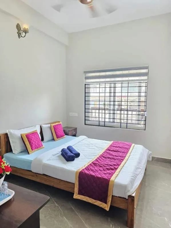 Uma cama de solteiro com cabeceira, janela com grades de metal e um ventilador de teto.