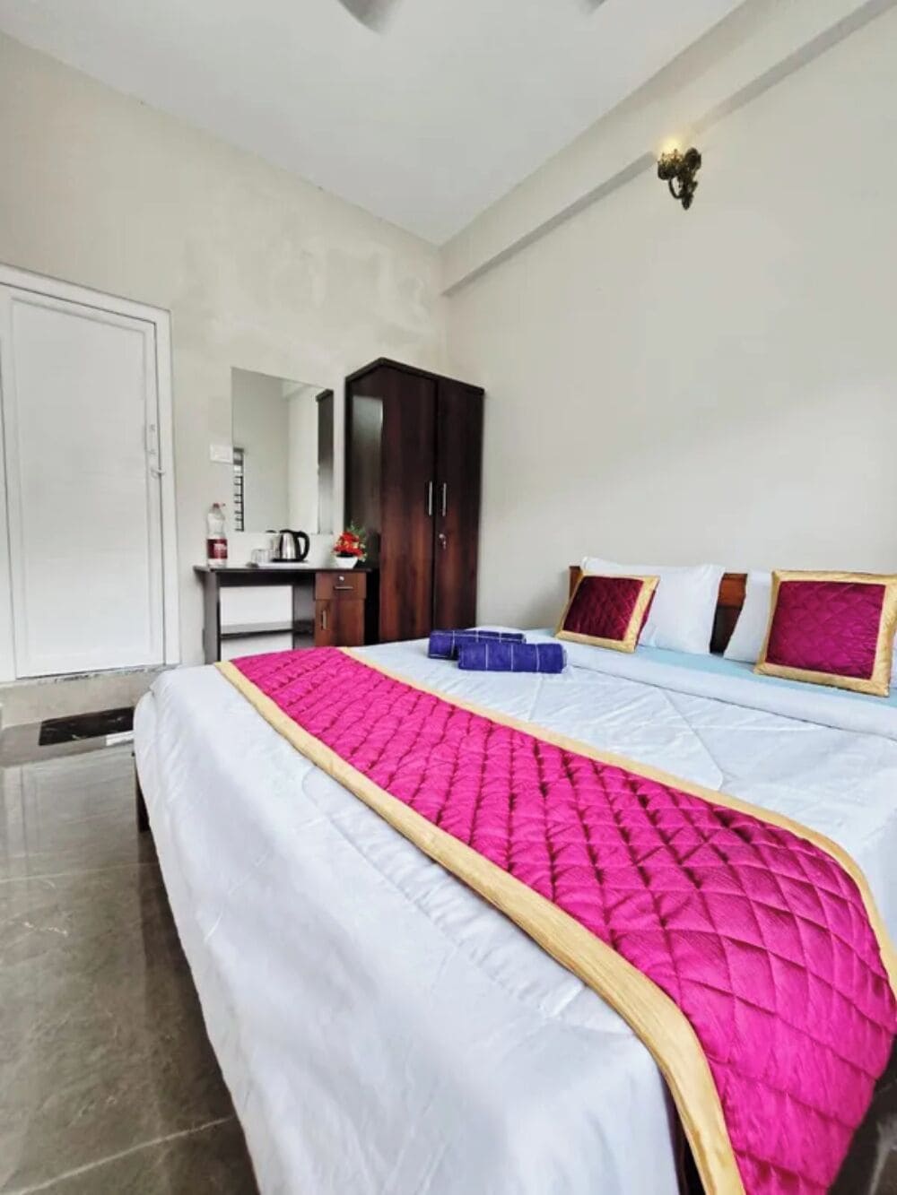 Habitación de hotel con cama, armario, escritorio con espejo y lámpara de pared.