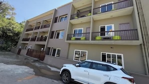 A multi-story residential building with balconies and a white car parked in front.