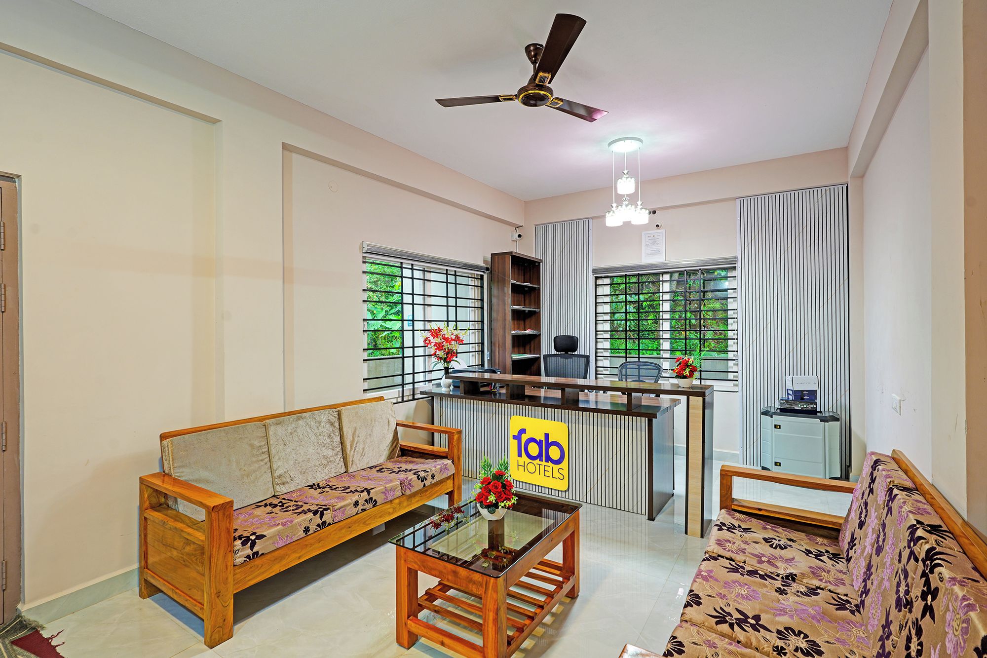 A hotel room with a kitchenette, two sofas, a glass coffee table, and a ceiling fan.