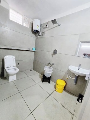 Casa de banho com sanita, lavatório, chuveiro e um balde amarelo.