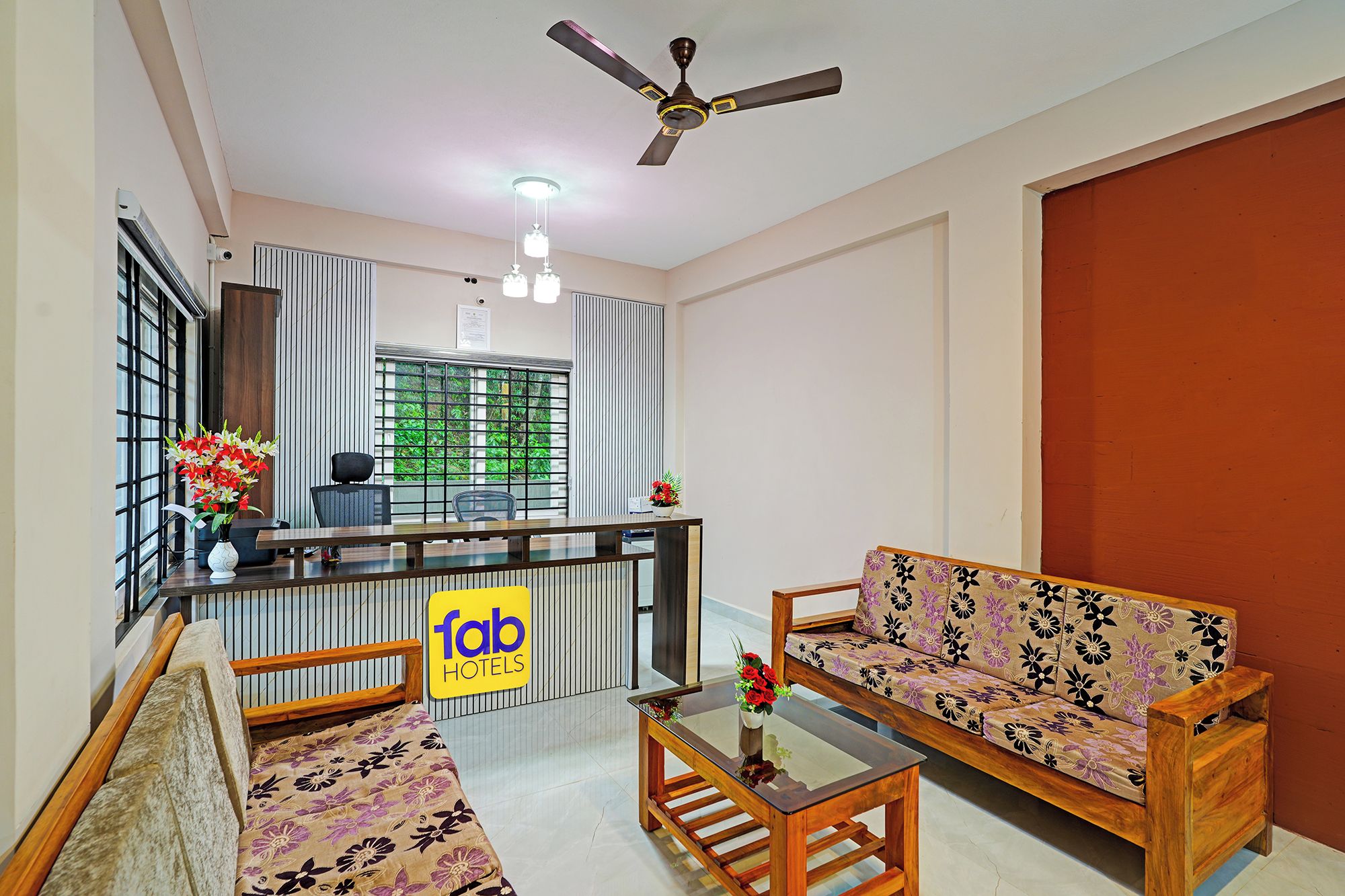 A hotel lobby with a reception desk, a sofa, a coffee table, and a ceiling fan.