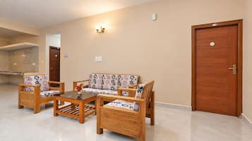 A room with a sofa set, two chairs, a coffee table, a wooden door, and a wall-mounted light fixture.