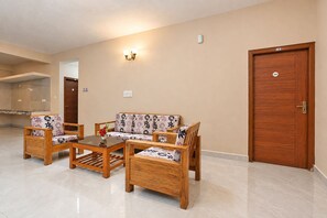 Ein Zimmer mit einer Sofagarnitur, zwei Stühlen, einem Couchtisch, einer Holztür und einer wandmontierten Leuchte.