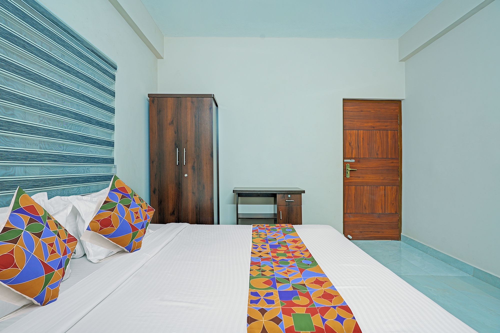 Een slaapkamer met een bed, een houten garderobe, een bureau en een deur.