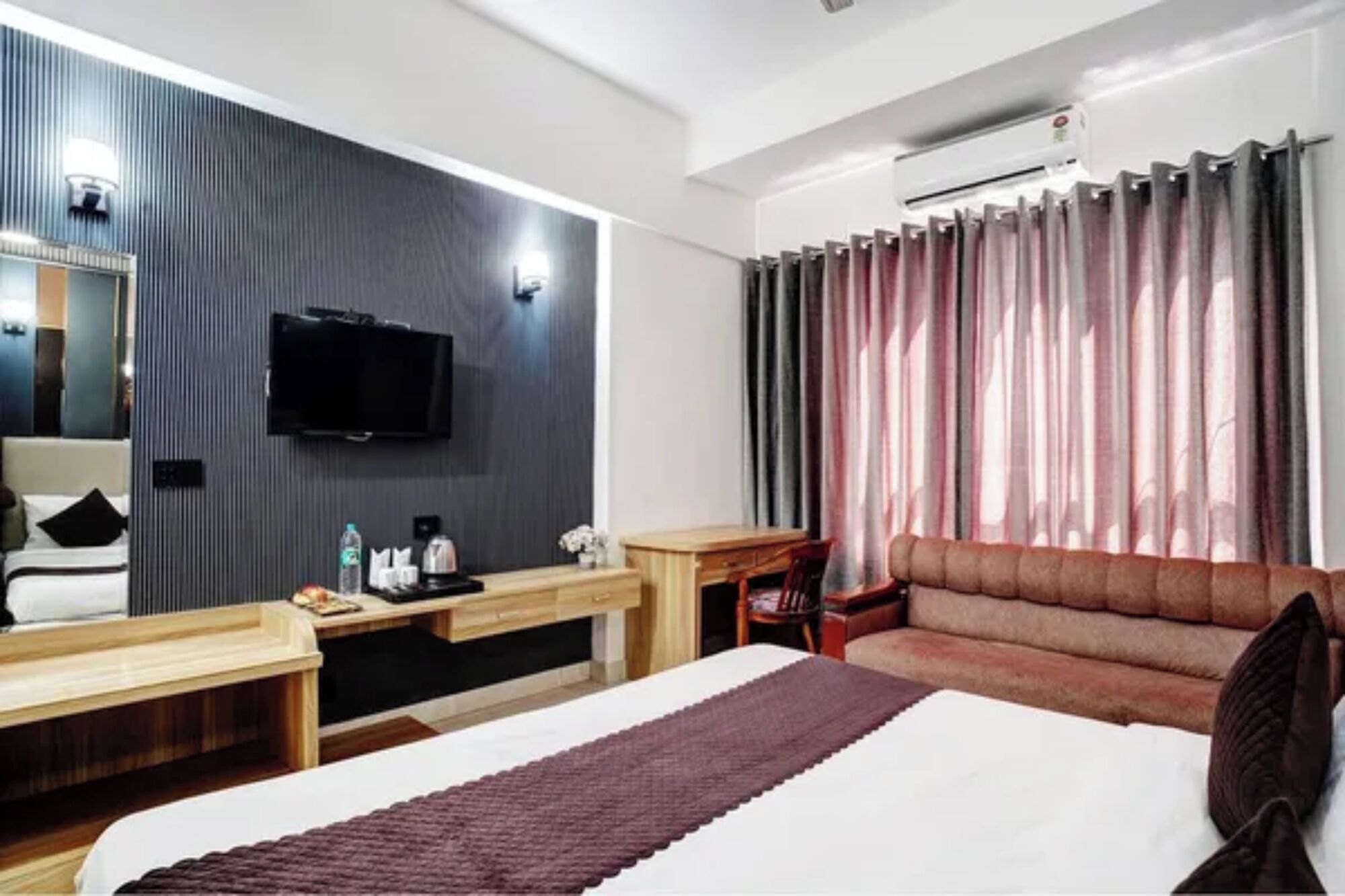 A hotel room with a bed, a desk, a chair, a television, and a window with curtains.