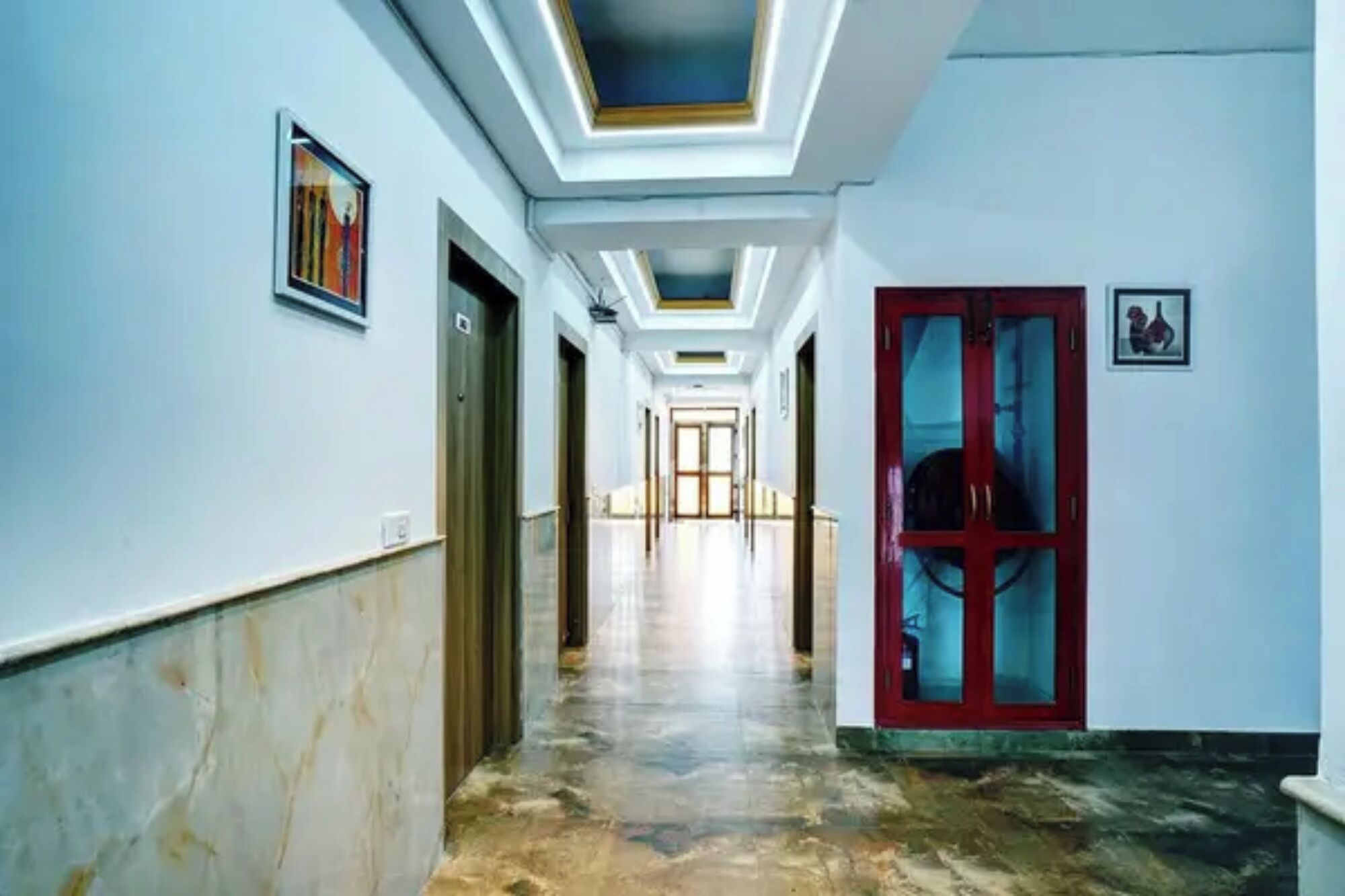 Un pasillo con suelo de mármol, puertas a la izquierda y una puerta roja a la derecha.