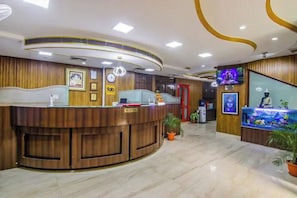 A reception area with a wooden reception desk, a clock, and a TV screen. - FabHotel Prime The Rivlet MG Road - MG Road (Gurugram)
