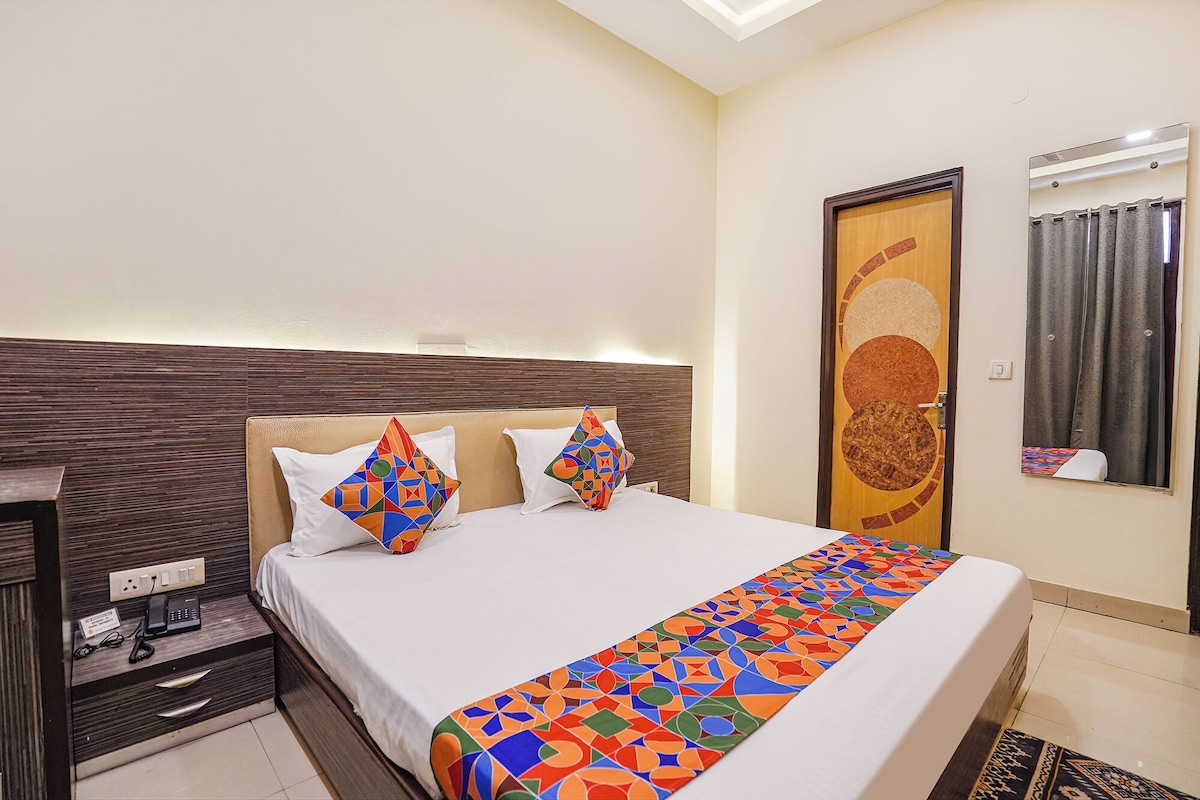 Una habitación de hotel con cama, mesita de noche, toma de corriente y una obra de arte en la pared.