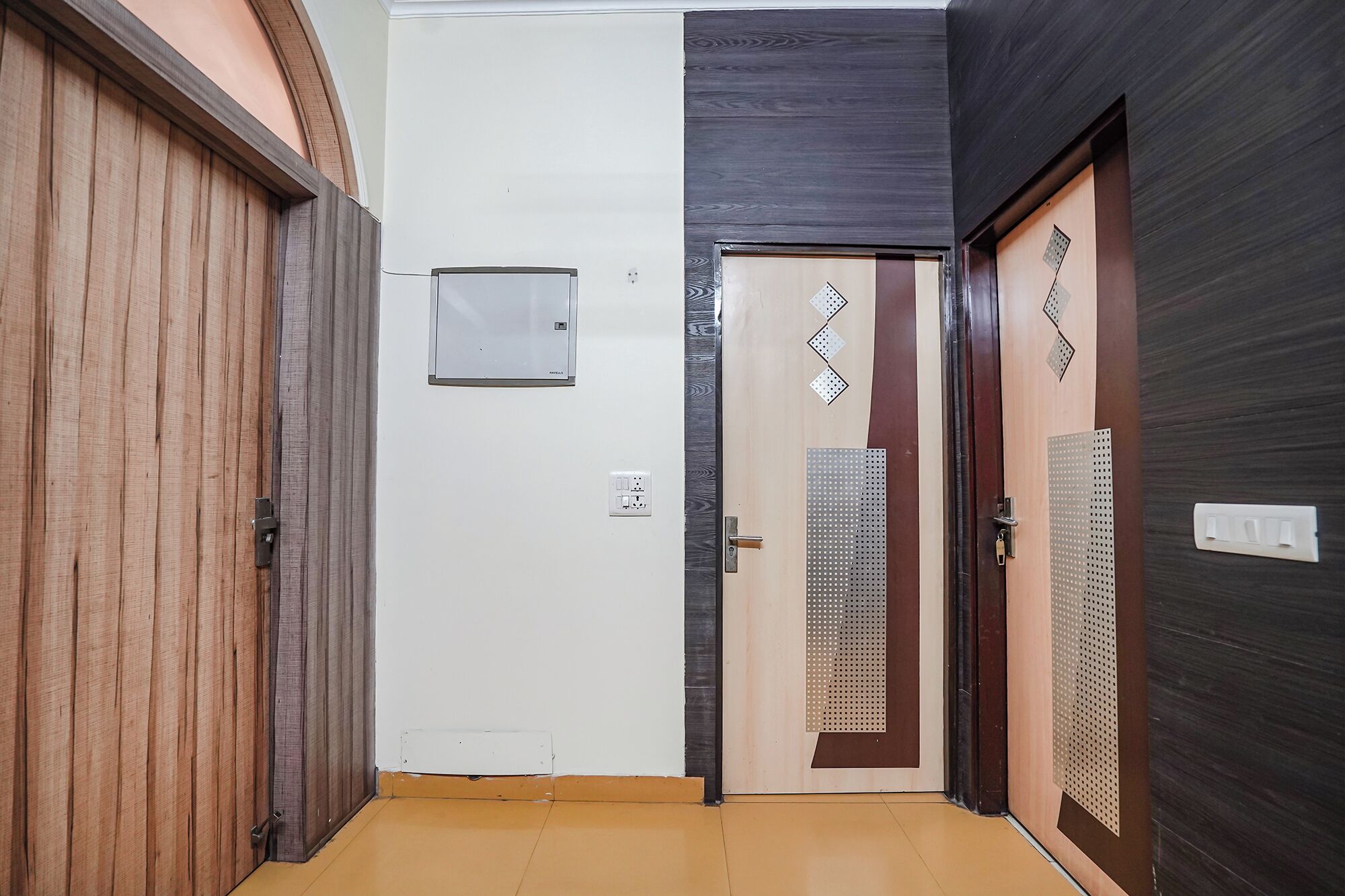 Un pasillo con una puerta de madera a la izquierda, una puerta blanca en el centro y una puerta de madera oscura a la derecha.