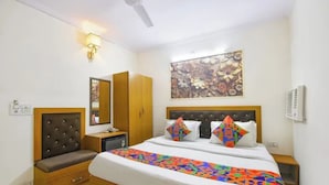 A hotel room with a bed, a nightstand, a wardrobe, a ceiling fan, a wall-mounted light, and a floral painting. - Fabhotel New Rivlet (New Delhi)