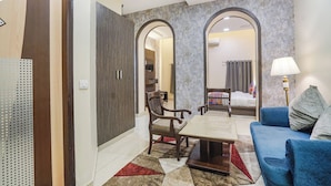 A hotel room with a sofa, a coffee table, a desk, and a chair. There is a mirror on the wall and a lamp on the side. - Fabhotel New Rivlet (New Delhi)