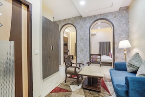 Habitación de hotel con sofá, mesa de centro, escritorio y silla. Hay un espejo en la pared y una lámpara al lado.