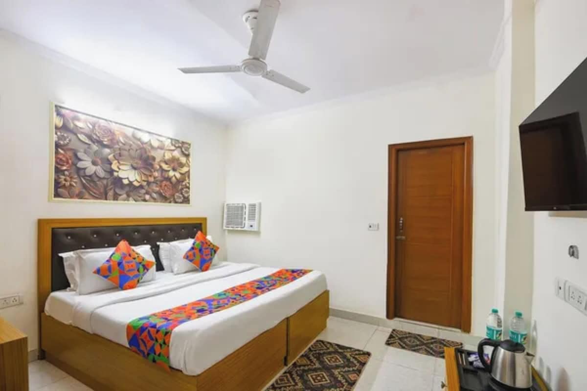 Habitación de hotel con cama, ventilador de techo, un cuadro, unidad de aire acondicionado, puerta de madera y televisión.