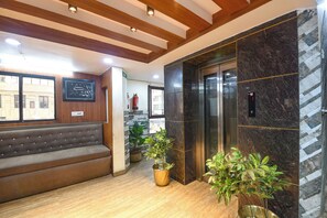 A lobby with a brown sofa, potted plants, an elevator, and a marble wall. - Fabhotel Rivlet Central (New Delhi)