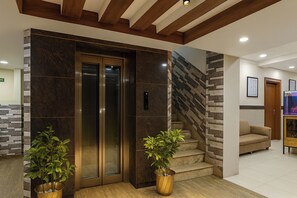 An interior with a modern elevator, a staircase with a geometric wall design, and a seating area with a sofa.