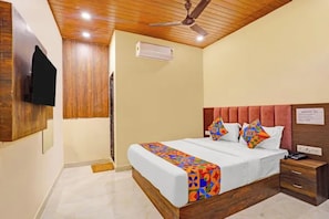 A bedroom with a wooden ceiling, a bed with colorful bedding, a nightstand, and a mounted television. - Via Surya Grand (Mumbai)