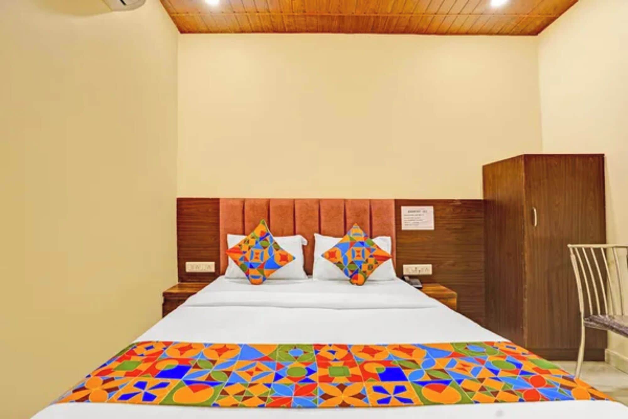 Habitación de hotel con cama, dos almohadas, cabecero de madera, armario y una silla.