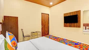Quarto com cama, escrivaninha, cadeira, televisão na parede e porta.