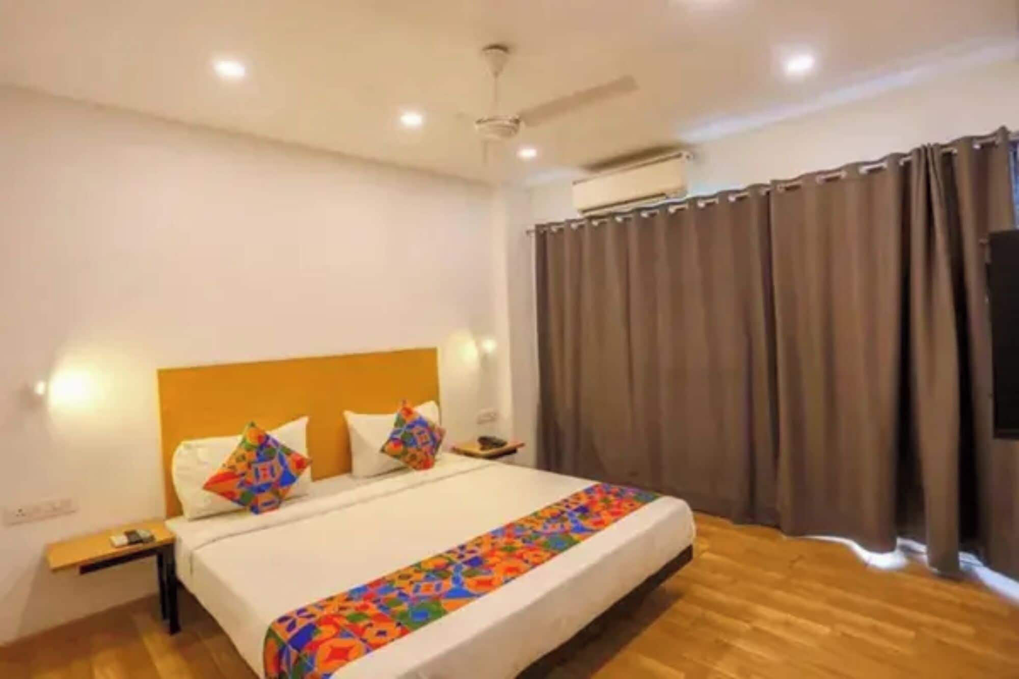 A hotel room with a bed, a bedside table, a nightstand, a ceiling fan, and a window with curtains.