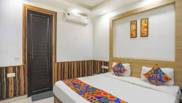 Una habitación de hotel con una cama, una puerta, un equipo de aire acondicionado y dos cuadros en la pared.