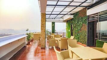 A rooftop terrace with wicker furniture, a glass ceiling, and a green wall with plants.