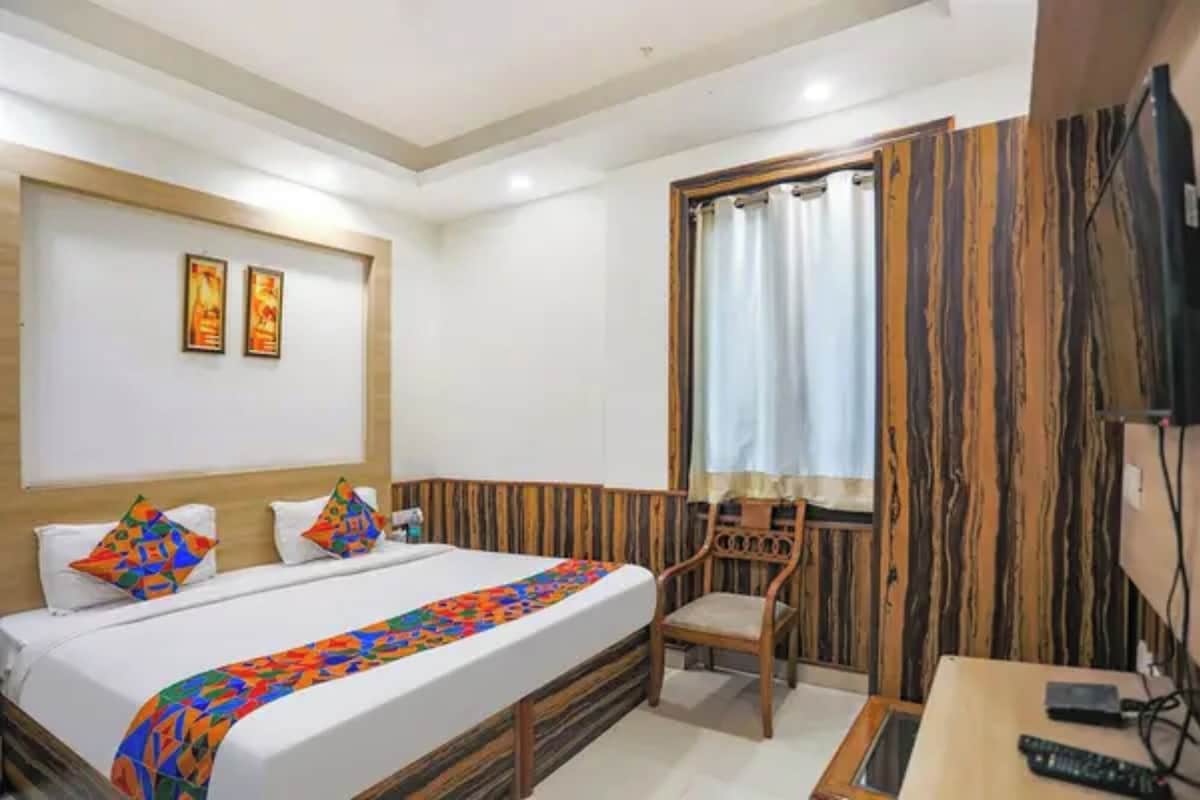 A hotel room with a bed, a chair, a television, and a window with curtains.