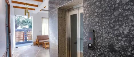 A hotel lobby with a marble reception desk, a glass elevator, and a seating area with a view of the outdoors.